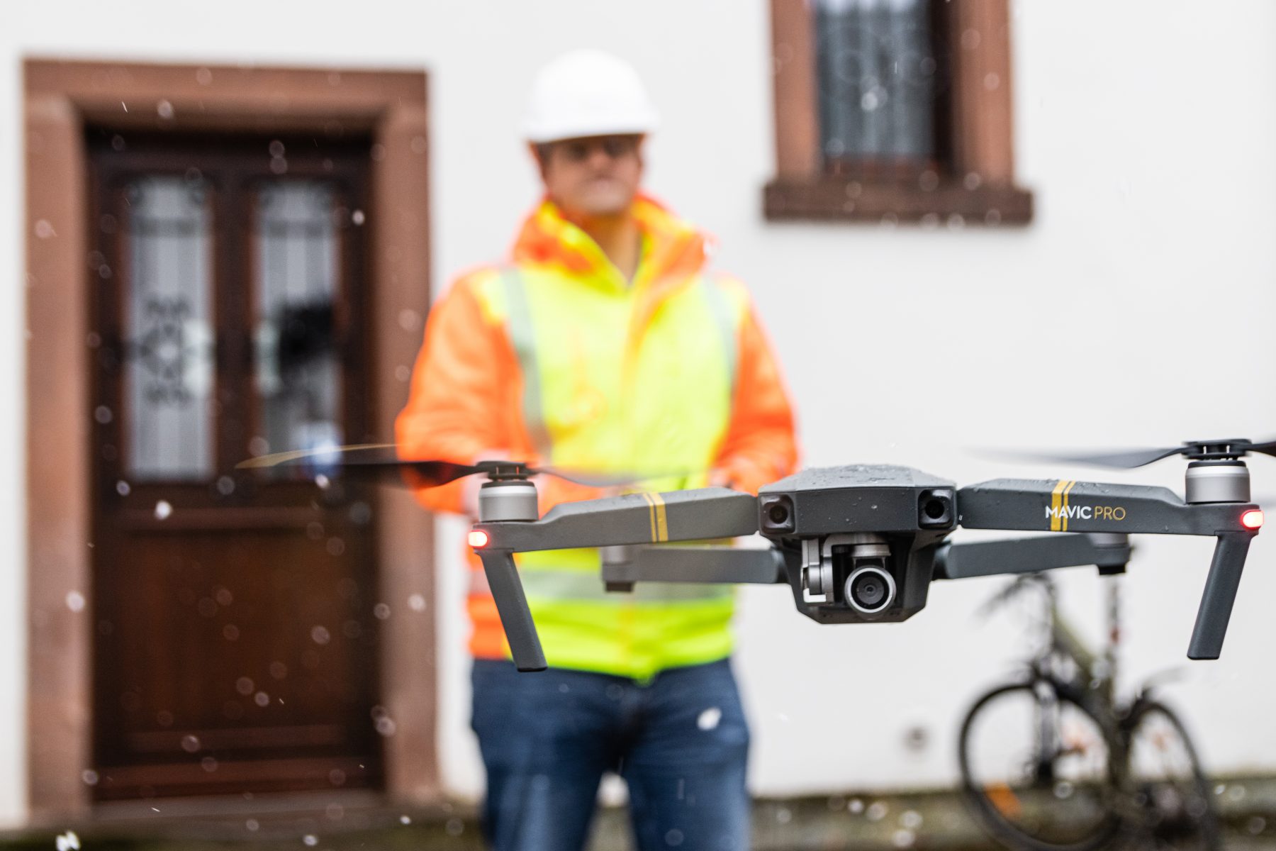 Das Bild zeigt eine Person mit Warnweste und Sicherheitskleidung im Hintergrund und eine Drohne im Vordergrund