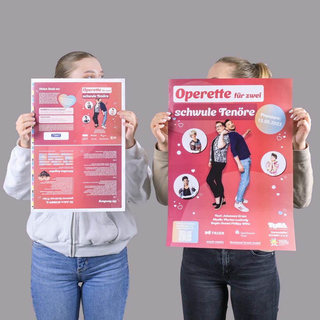 Bild zeigt zwei Personen, die ein Plakat und einen Druckbogen in den Händen halten