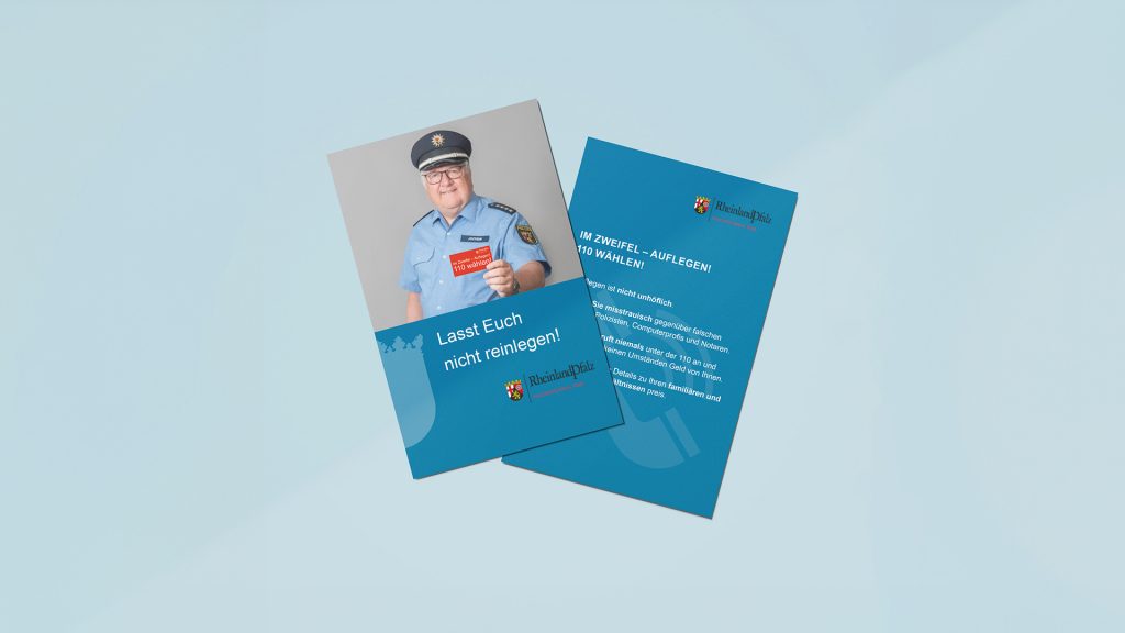 Plakat, das einen Polizisten abbildet, der eine Karte in die Kamera hält, auf der "Im Zweifelsfall 110 wählen" steht. Als Titel des Plakates unter dem Foto steht "Lasst Euch nicht reinlegen!" zusammen mit einer Rückseite mit näheren Informationen.