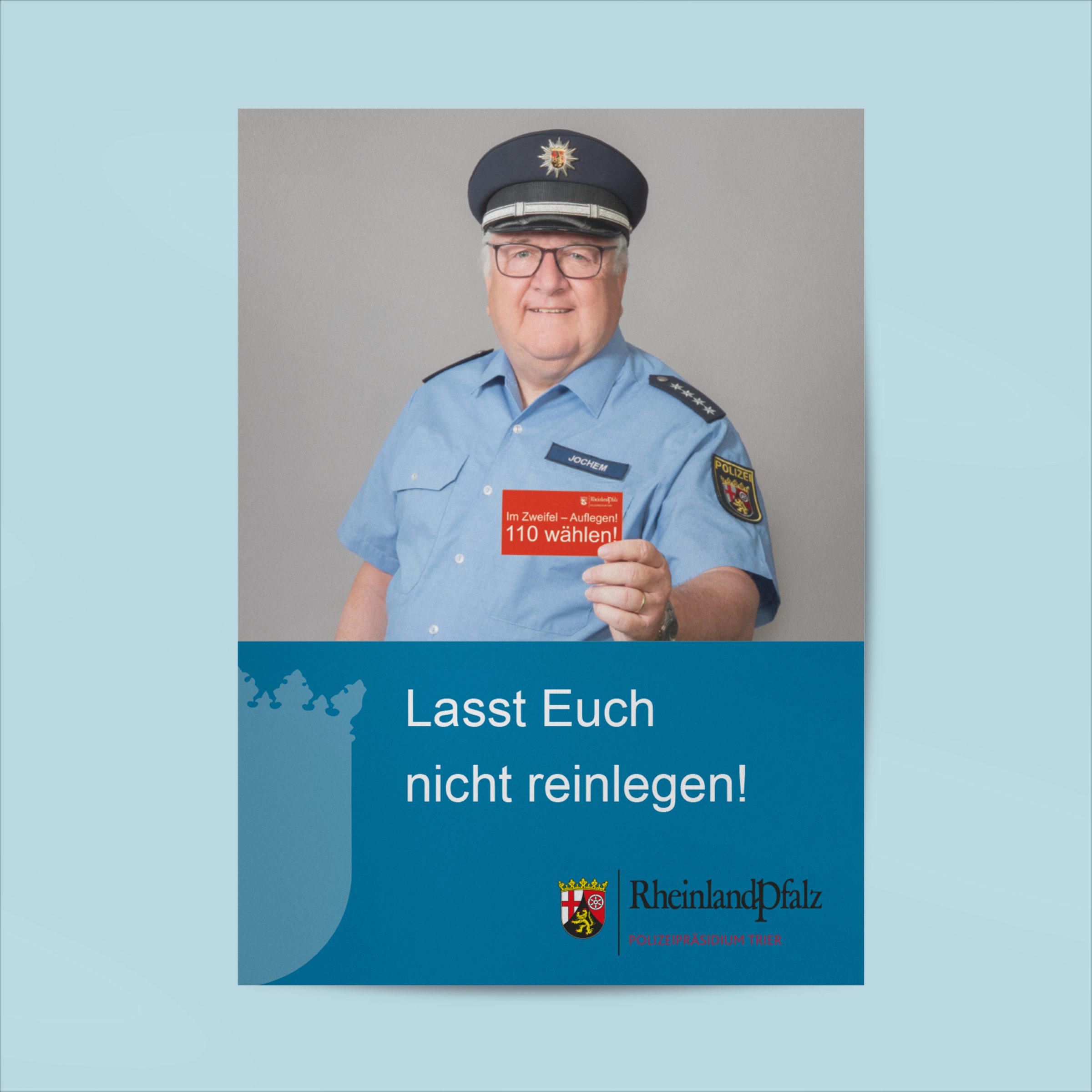 Plakat, das einen Polizisten abbildet, der eine Karte in die Kamera hält, auf der "Im Zweifelsfall 110 wählen" steht. Als Titel des Plakates unter dem Foto steht "Lasst Euch nicht reinlegen!"