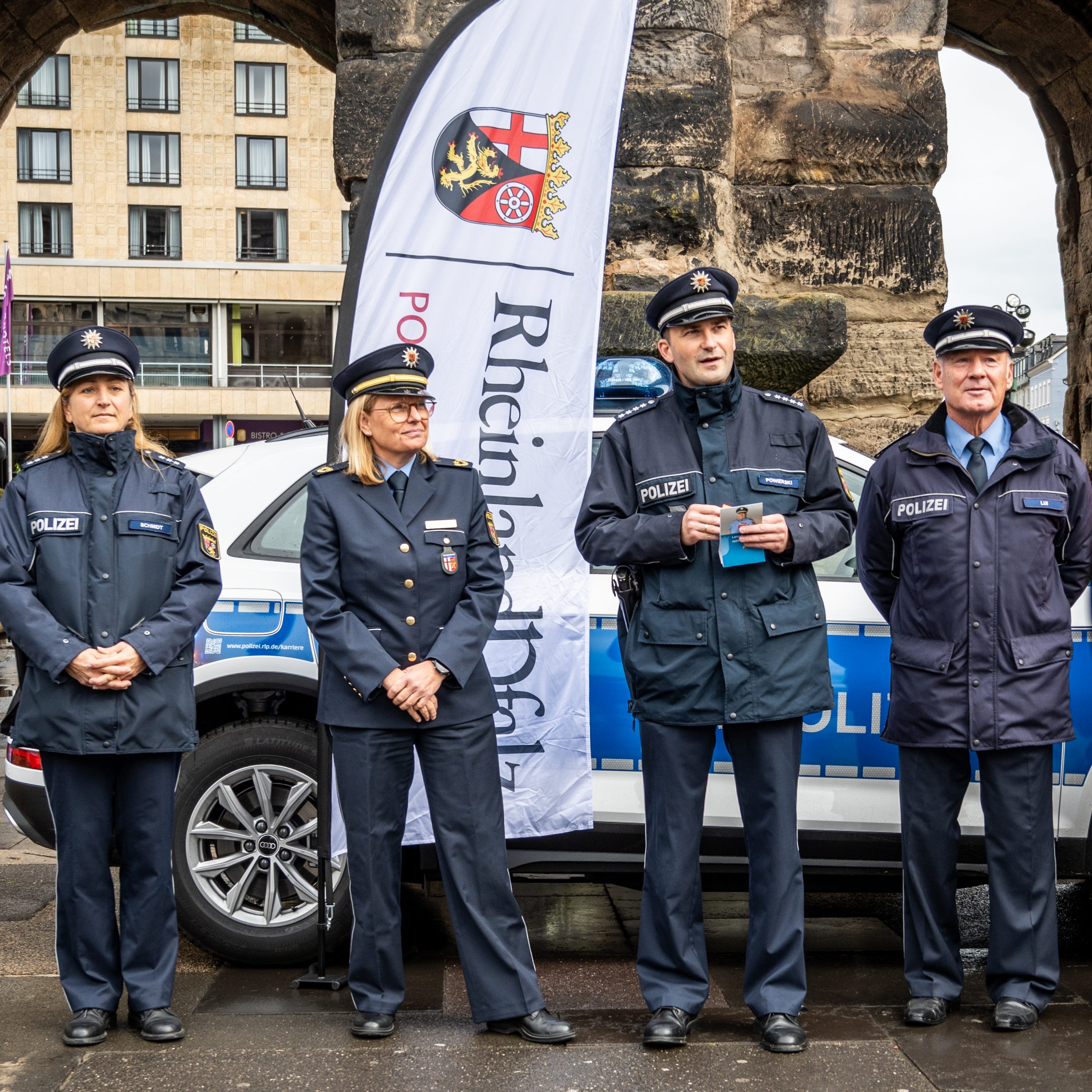 Vier Polizisten und Polizistinnen stehen nebeneinander vor einem Polizeiauto, das an der Porta Nigra steht.