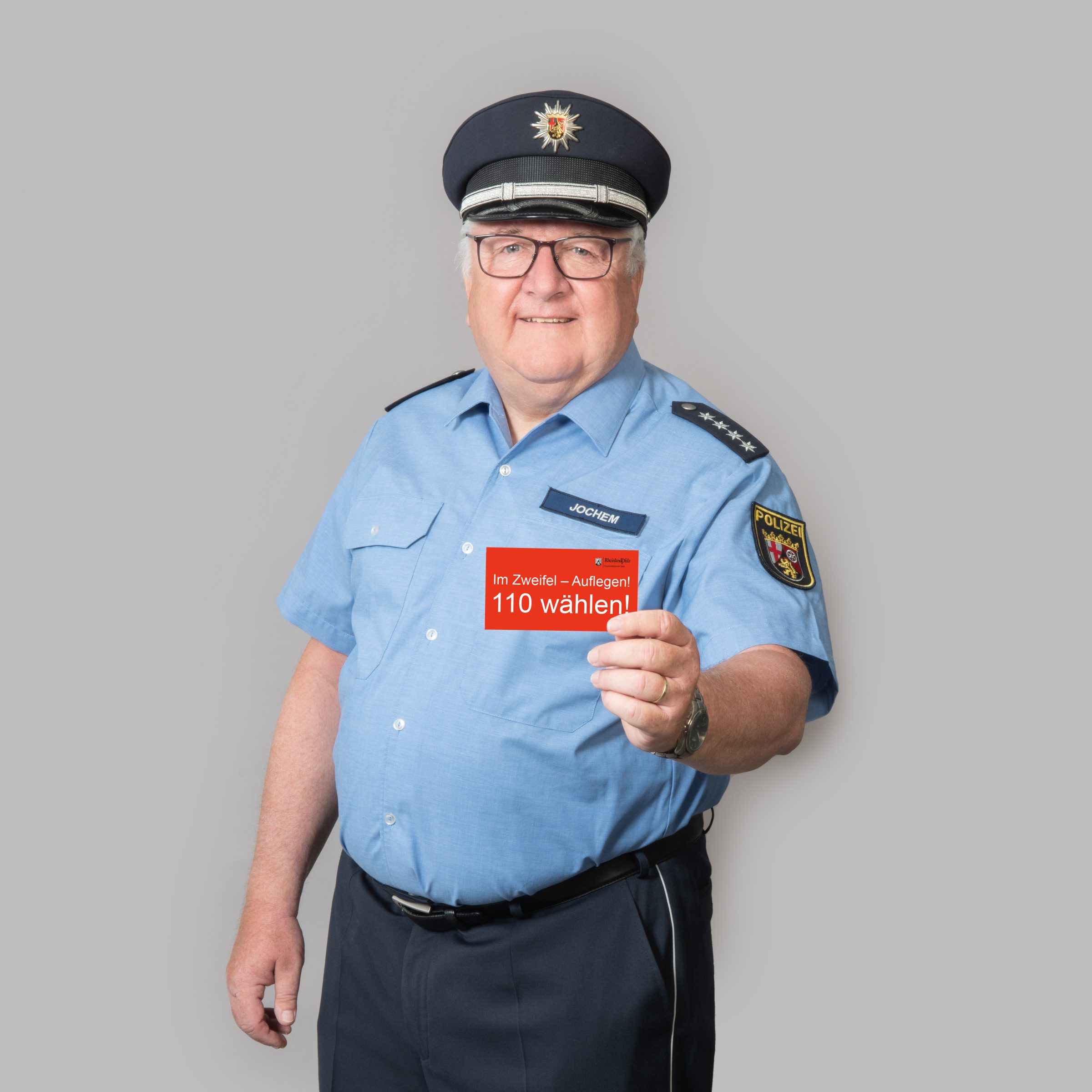 Foto, das einen Polizisten abbildet, der eine Karte in die Kamera hält, auf der "Im Zweifelsfall 110 wählen" steht.