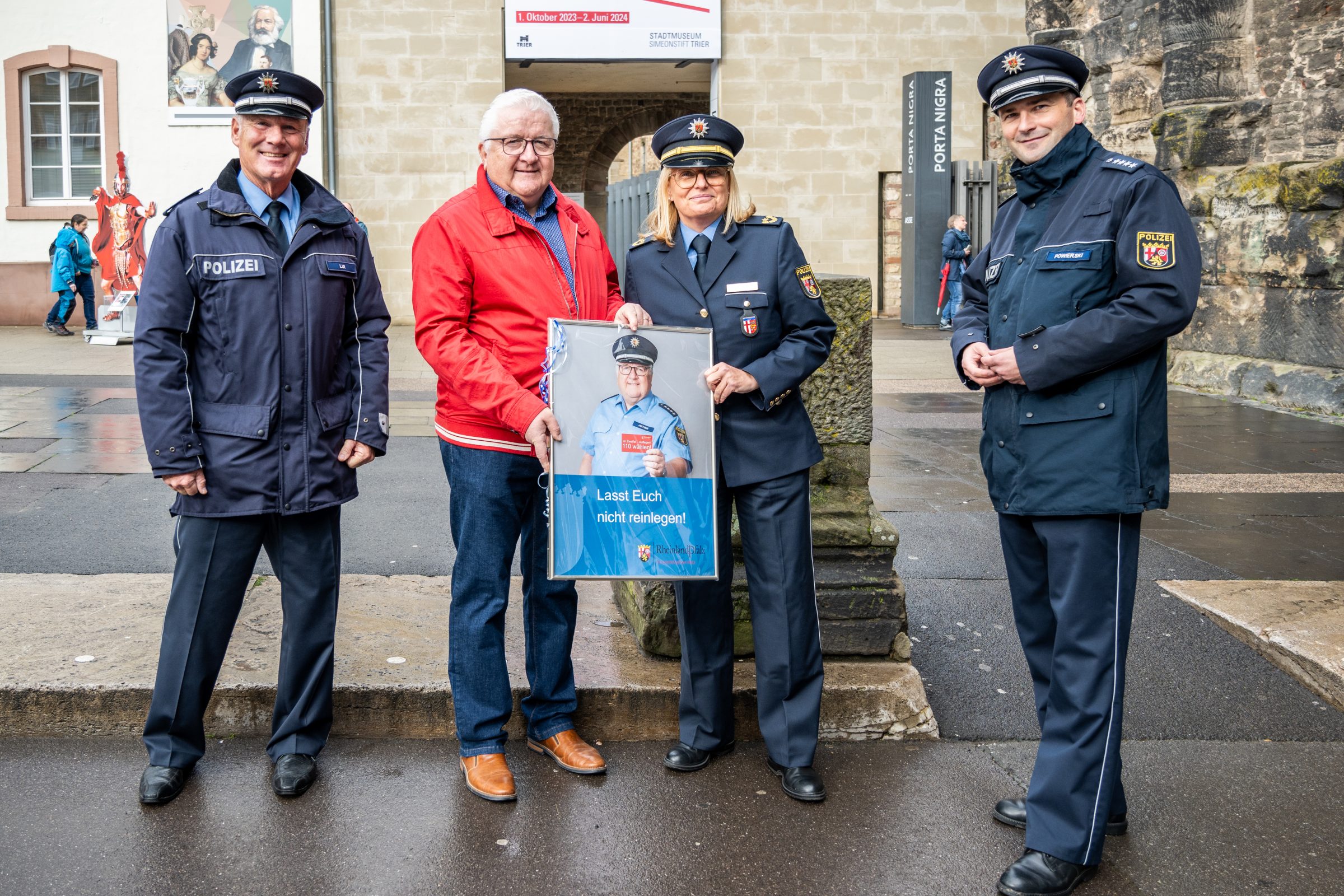Vier Polizisten und Polizistinnen stehen im Kreis und freuen sich über ein Geschenk, welches das Plakat für die Polizei eingerahmt ist.